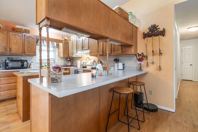 kitchen featuring light wood finished floors, a peninsula, decorative backsplash, black microwave, and a kitchen bar