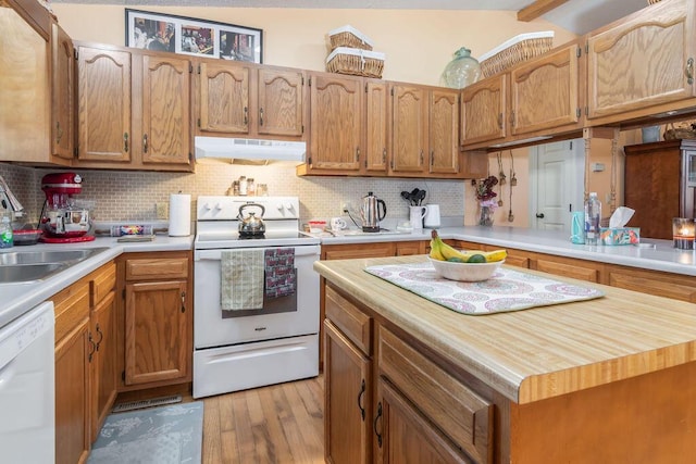 kitchen featuring white appliances, a sink, light wood-style floors, under cabinet range hood, and tasteful backsplash