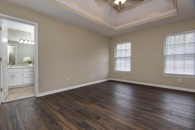 unfurnished bedroom featuring wood finished floors, baseboards, ensuite bath, a tray ceiling, and crown molding