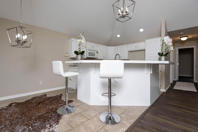 kitchen featuring white cabinetry, a kitchen breakfast bar, white microwave, and vaulted ceiling