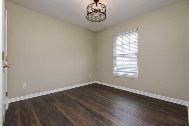 spare room featuring dark wood finished floors, visible vents, a notable chandelier, and baseboards