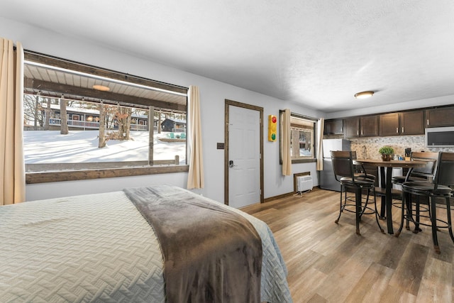 bedroom featuring heating unit, light wood-style flooring, a textured ceiling, and freestanding refrigerator