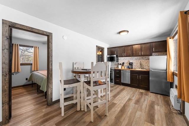 kitchen featuring dark brown cabinetry, decorative backsplash, light wood-style flooring, appliances with stainless steel finishes, and a sink