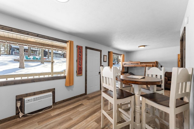 dining room with a wall unit AC, wood finished floors, baseboards, and a textured ceiling