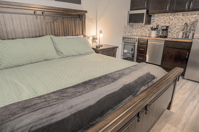 bedroom with a sink, freestanding refrigerator, and light wood finished floors