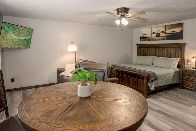 bedroom with ceiling fan, wood finished floors, baseboards, and a textured ceiling