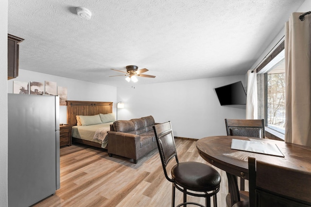 bedroom with a textured ceiling, freestanding refrigerator, light wood-style floors, and a ceiling fan