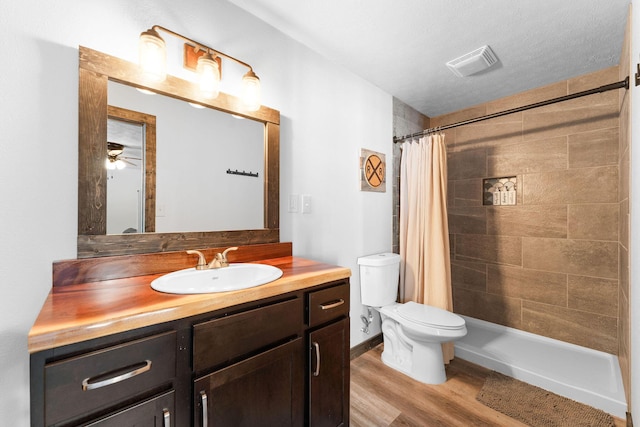 full bathroom with visible vents, toilet, a tile shower, wood finished floors, and vanity