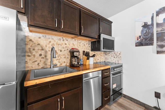 kitchen featuring a sink, tasteful backsplash, stainless steel appliances, dark brown cabinetry, and light wood finished floors