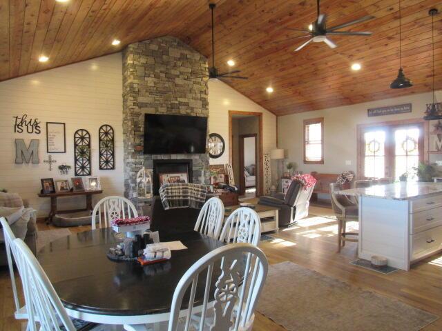 dining area featuring a stone fireplace, wood finished floors, wood ceiling, and a ceiling fan