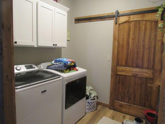 laundry room featuring cabinet space, independent washer and dryer, light wood-style flooring, and a barn door