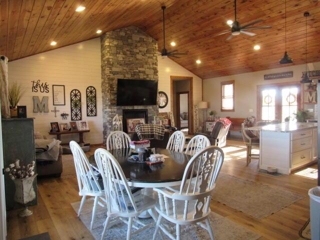 dining area featuring ceiling fan, wood ceiling, light wood-type flooring, a stone fireplace, and high vaulted ceiling