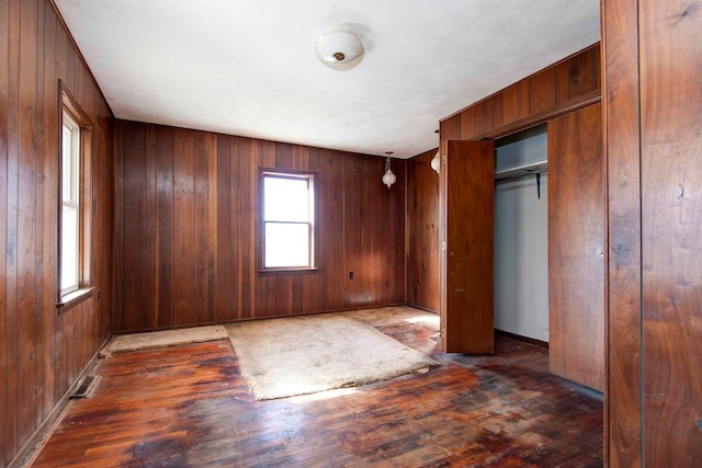 unfurnished bedroom featuring a closet, wood-type flooring, wooden walls, and baseboards