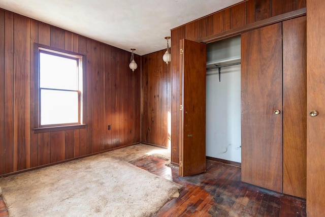 unfurnished bedroom with a closet, wooden walls, baseboards, and hardwood / wood-style floors