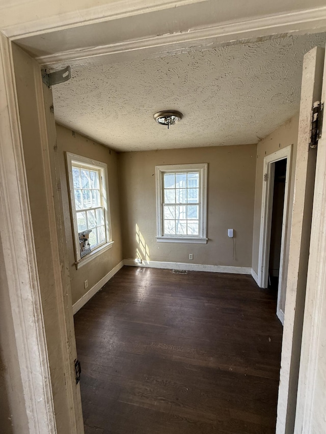 unfurnished room featuring a textured ceiling, dark wood-type flooring, and baseboards