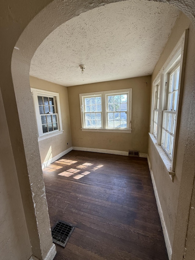 empty room with visible vents, baseboards, arched walkways, wood-type flooring, and a textured ceiling