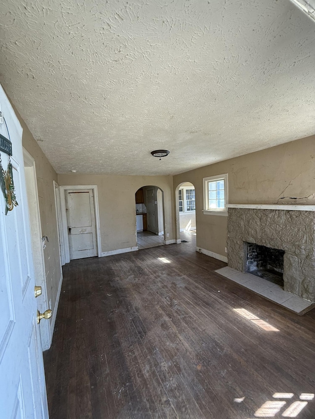 unfurnished living room with baseboards, arched walkways, a stone fireplace, and hardwood / wood-style flooring