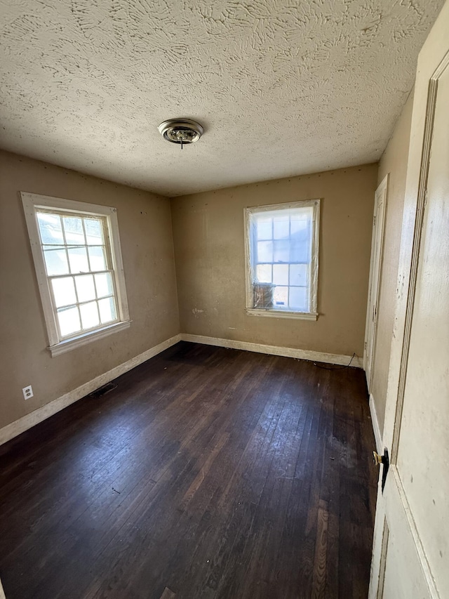 empty room featuring dark wood-type flooring, baseboards, visible vents, and a wealth of natural light