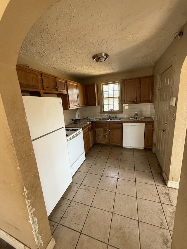 kitchen featuring white appliances, light tile patterned floors, brown cabinets, and backsplash