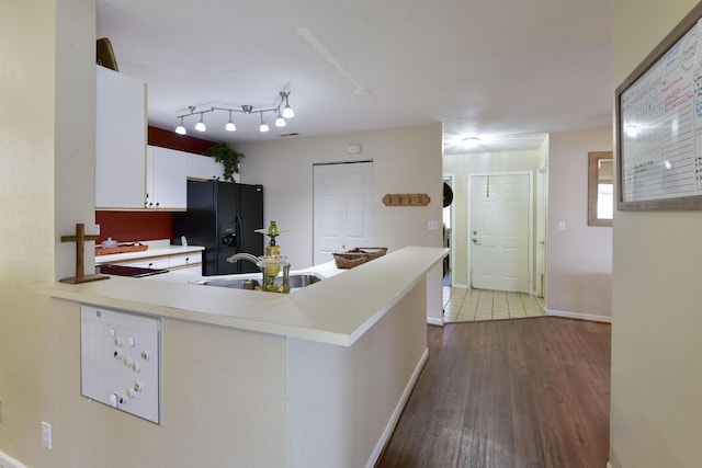 kitchen with black fridge, a sink, wood finished floors, white cabinets, and light countertops