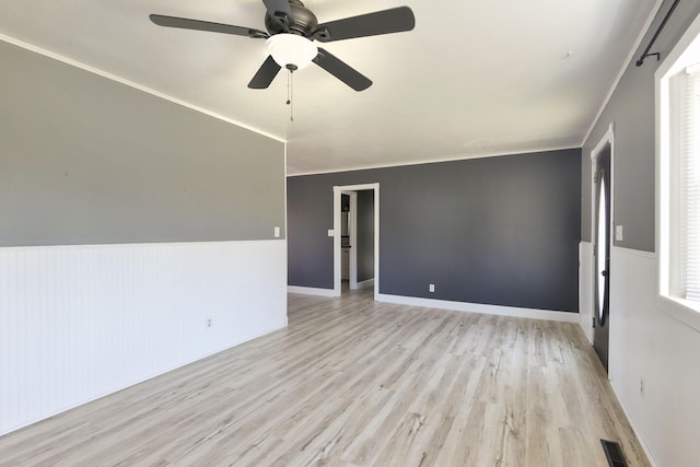 spare room with light wood-type flooring, visible vents, a ceiling fan, and wainscoting