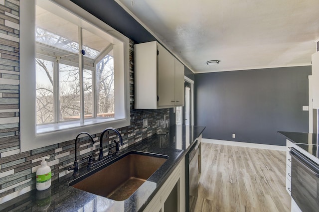 kitchen featuring tasteful backsplash, a sink, baseboards, light wood-style flooring, and stainless steel dishwasher