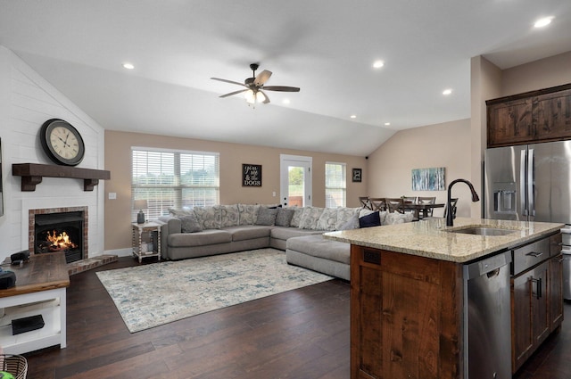 kitchen with light stone counters, lofted ceiling, a sink, stainless steel appliances, and dark wood-type flooring