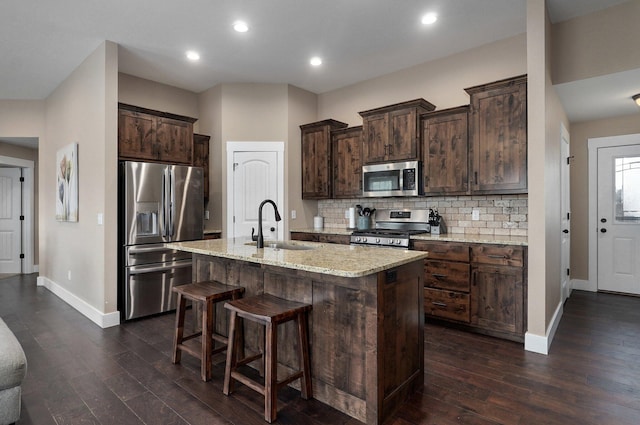 kitchen with a breakfast bar, a sink, stainless steel appliances, dark brown cabinetry, and backsplash