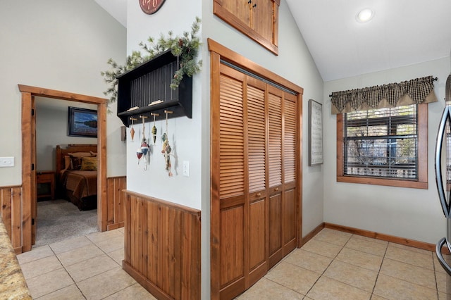 corridor with light tile patterned floors, wooden walls, wainscoting, and vaulted ceiling