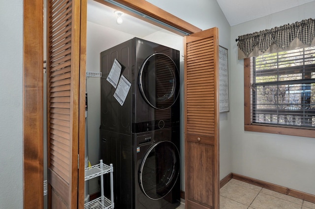 clothes washing area with tile patterned floors, baseboards, stacked washer / drying machine, and laundry area