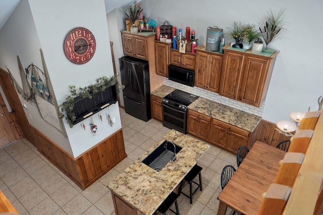 kitchen featuring brown cabinetry, decorative backsplash, black appliances, and light tile patterned floors