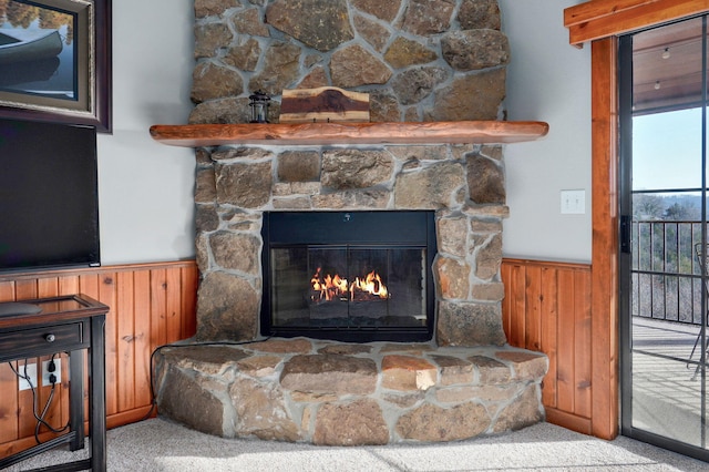 room details featuring a wainscoted wall, a stone fireplace, wood walls, and carpet flooring