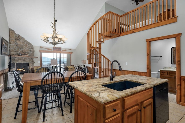 kitchen featuring brown cabinetry, a sink, a stone fireplace, black dishwasher, and open floor plan