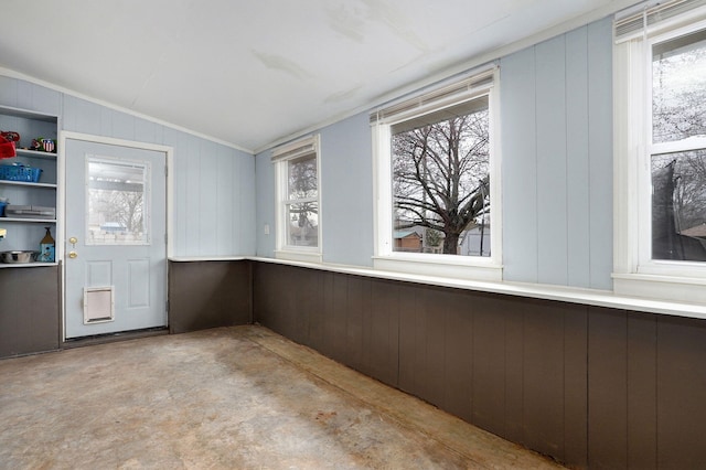 spare room featuring concrete floors, lofted ceiling, wood walls, and a wealth of natural light