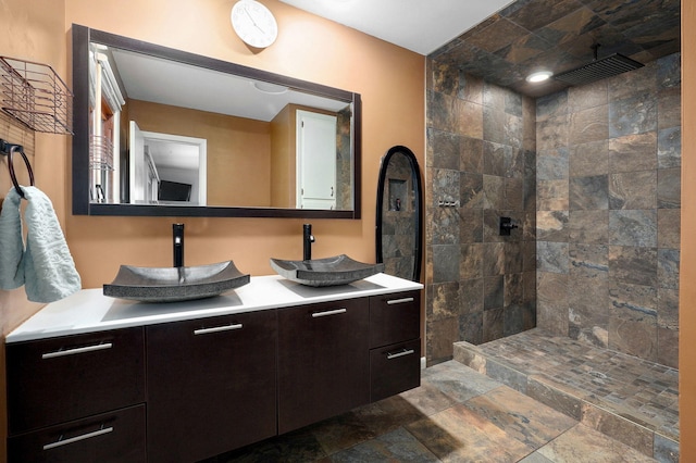 bathroom featuring a sink, stone finish flooring, double vanity, and a walk in shower