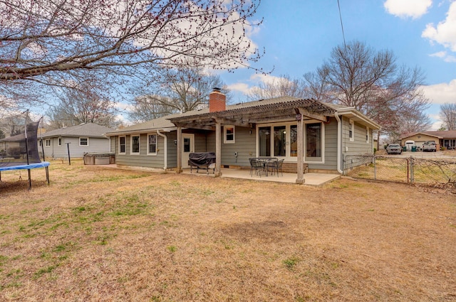 rear view of property featuring a gate, a trampoline, fence, a chimney, and a patio area