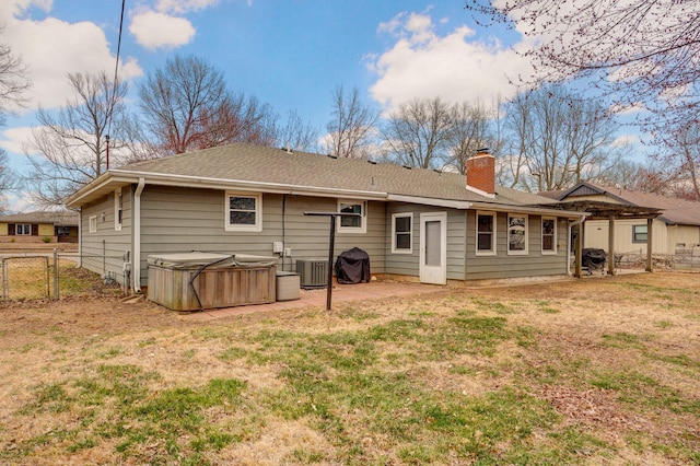 rear view of house with a hot tub, fence, a chimney, a yard, and a patio area