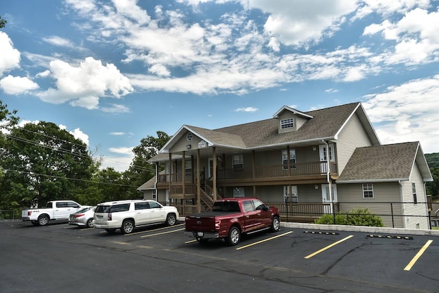 view of front facade featuring a shingled roof, fence, and uncovered parking