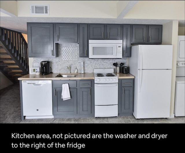 kitchen featuring white appliances, visible vents, gray cabinetry, a sink, and stacked washer and dryer