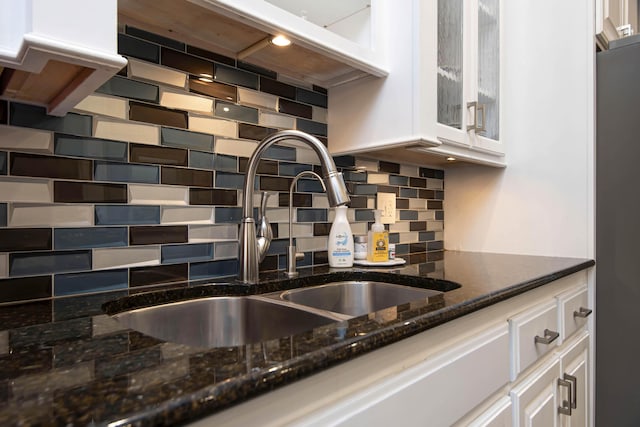 interior space with tasteful backsplash, dark stone countertops, freestanding refrigerator, white cabinets, and a sink