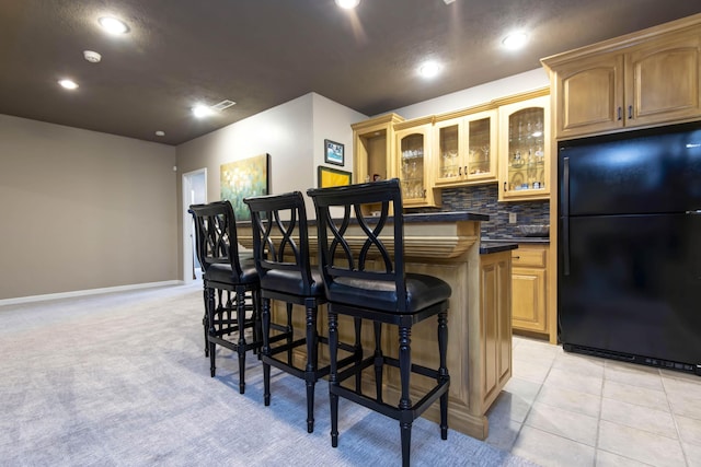 kitchen featuring dark countertops, glass insert cabinets, a breakfast bar, decorative backsplash, and freestanding refrigerator