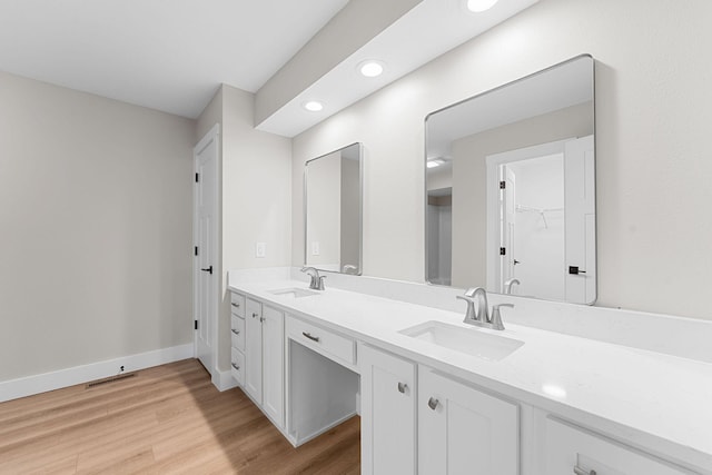 full bath featuring double vanity, wood finished floors, baseboards, and a sink