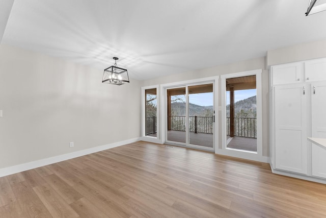 unfurnished dining area featuring a chandelier, a mountain view, baseboards, and light wood-style floors