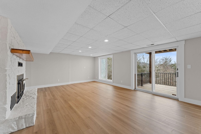 unfurnished living room with a drop ceiling, light wood-type flooring, baseboards, and a stone fireplace