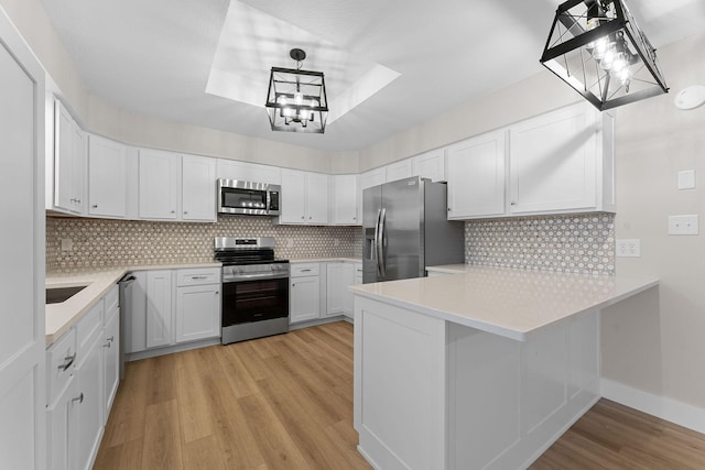 kitchen with light wood finished floors, appliances with stainless steel finishes, light countertops, and a peninsula