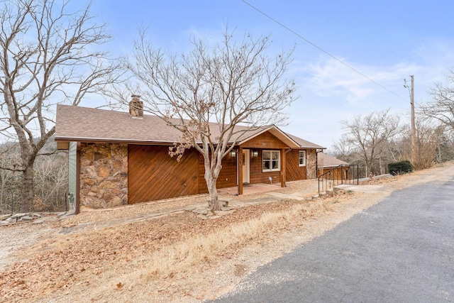 view of front of home featuring driveway, a porch, a chimney, a shingled roof, and stone siding