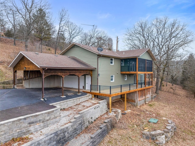 back of house with aphalt driveway, a shingled roof, a carport, and a sunroom