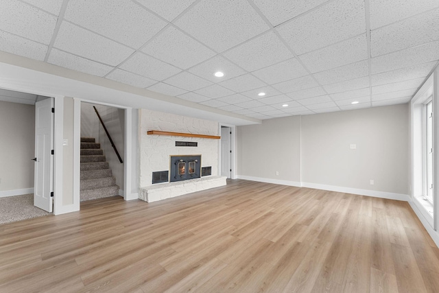 unfurnished living room with stairway, light wood-style floors, baseboards, and a paneled ceiling