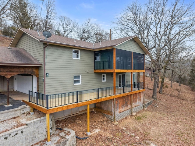 rear view of house featuring a deck, aphalt driveway, roof with shingles, a sunroom, and a garage