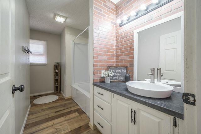 bathroom featuring a textured ceiling, wood finished floors,  shower combination, baseboards, and vanity